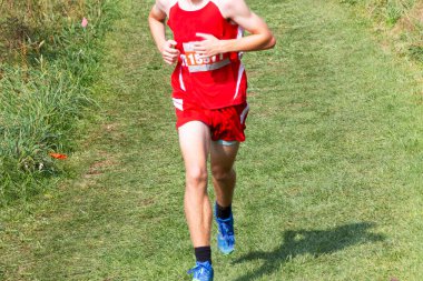 Bir liseli çocuk, Bowdoin park New York 'taki 5K yarışı sırasında yokuş aşağı çim tarlasında tek başına koşuyor..