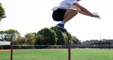 Bir lise sporcusu atletizm antrenmanında bir çim sahasına yerleştirilmiş engellerin üzerinden atlıyor..