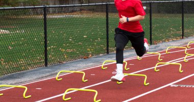 Lisedeki atletizm koşucusu koşu antrenmanı sırasında sarı 15 santimlik küçük muz engellerini aşıyor..