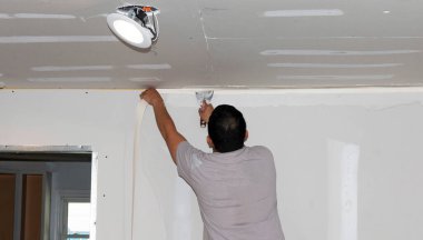 Ev yenilenmesi sırasında yeni alçıpan duvarlara ve tavana alçı bandı yapıştıran bir müteahhitin arka görünümü.