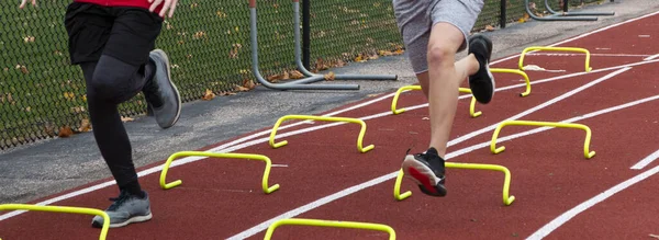 Nogi Dwóch Licealistów Przebiegających Przez Żółte Mini Płotki Czerwonym Torze — Zdjęcie stockowe
