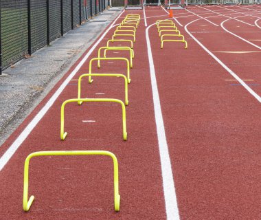 A high school track is set up with two lanes of different sized yellow hurdles in the outside lanes for speed and agility practice.