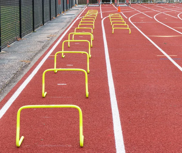 A high school track is set up with two lanes of different sized yellow hurdles in the outside lanes for speed and agility practice.