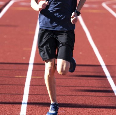 One high school boy running during track and field practice on a red track close up.