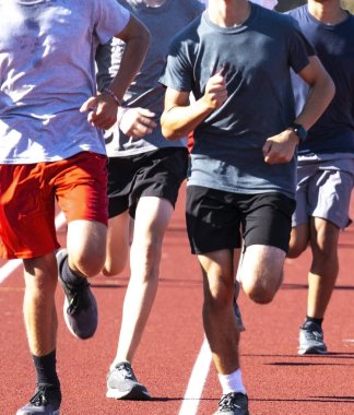 Close up of a front view of high school boys running togeher on a track during track and field practice in the spring.