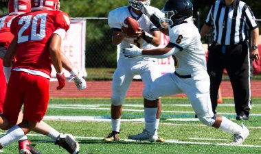 High school Quarterback handing off to his running back during a football game with defenders trying to stop him.