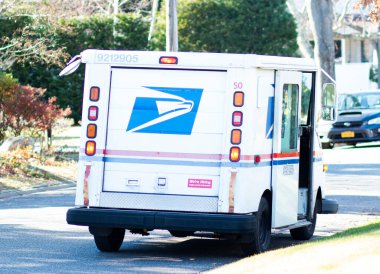 Babylon, New York, USA - 12 December 2021: A united States Postal Delivery truck is parked on a residential street in Babylon Village while the postal carrier is delivering the mail.