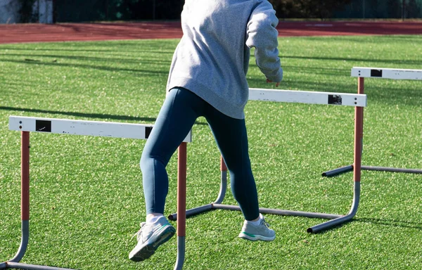 Rear view of a high school Hurdle runner perfoeming the trail leg drill on a turf field.
