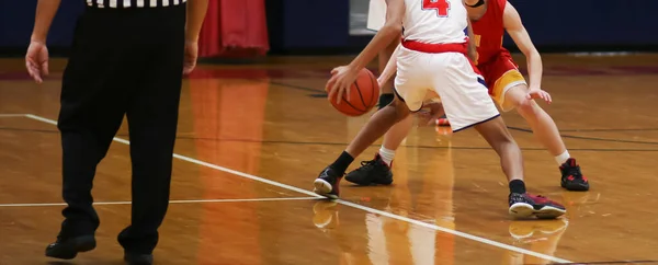 Rear view of a high school bay basketball player dribbling the ball making a move on the defender with the official watching