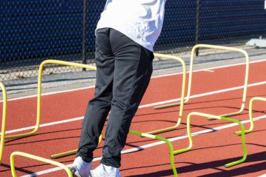 Liseli bir çocuk, bir pistte plastiğin üzerinden atlamak üzere..