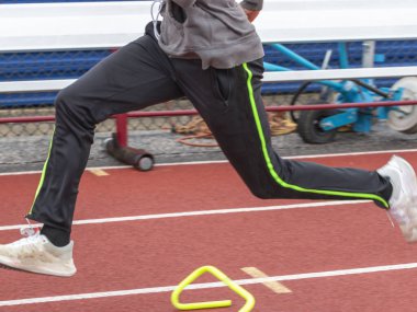 Bir lise atletizm koşucusu, kale hızlandırma tatbikatını yaparken küçük plastik engelleri aşıyor..