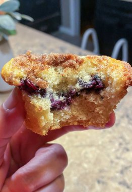 Bir insan eli taze bir yaban mersinli keki tutuyor ve onu ısırıyor..