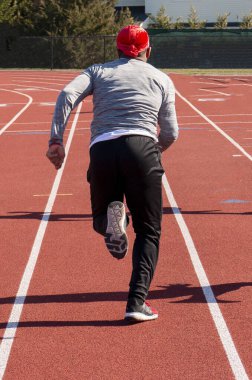 Pistte hızla koşan liseli bir koşucunun arkadan görünüşü.