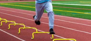 Kırmızı bir pistte sarı engelli koşan liseli bir çocuğun ön görüntüsü..