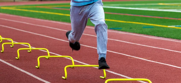 Kırmızı bir pistte sarı engelli koşan liseli bir çocuğun ön görüntüsü..