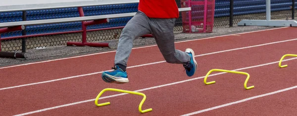 一个高中男孩在跑道上冲过一个黄色的小障碍物 — 图库照片