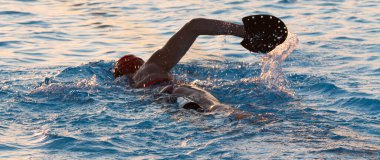 Sabahın erken saatlerinde triatlon antrenmanı sırasında eline büyük bir kürek takarak havuzda yüzen bir kadının arka görüntüsü..