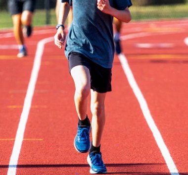 Bahar antrenmanı sırasında kırmızı pistte koşan liseli bir çocuğun ön görüntüsü..