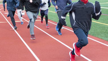 Bir grup liseli çocuğun soğuk bir öğleden sonra eşofman üstü ve eldiven giyerek pistte koşuşunun ön görüntüsü..