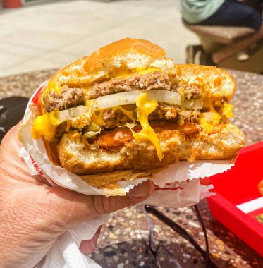 Elinde In-n-Out çizburgeriyle dışarıda yemek yerken yakın çekim yapan bir adam..