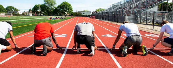 Rear view of five high school boys in the on your mark position in lanes on a track ready to sprint and run fast.