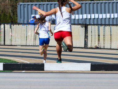Rear view of  High school girls competing in the steeplechase with one pushing off the steeple into the water pit. 