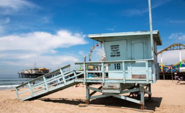 A light blue lifguard stand on the beach in Santa Monica California with the pier and its rides in the background.