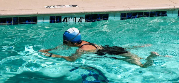 A women wearing goggles and swim cap while swimming the breast stroke in a hotel pool.