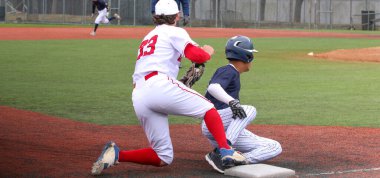 A high school baseball player sliding into third base with third baseman applying the tag during a game.