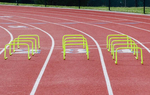 Three rows of yellow mini hurdles set up on a red track for runners agility practice.
