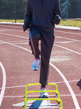Front view ofr a runner in the A-Position standing over yellow mini banana hurdles on a track.