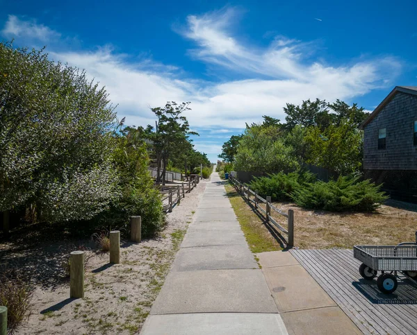 Looking down a cement walkway between summer homes that leads to a path over the sand dunes endig up on the beach at the Atlantic Ocean on Fire Island New York.