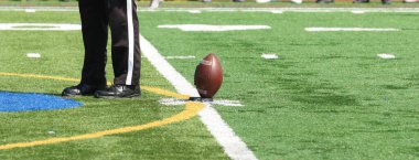 Yeşil çim sahasında bir lise maçının başlama vuruşunda üç hakem topun yanında duruyor..