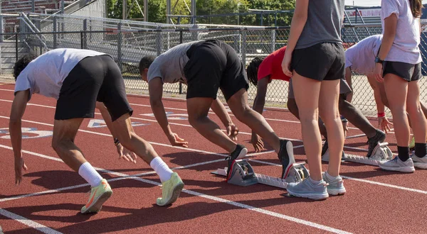 High school track runners starting a sprint race from the blocks at practice