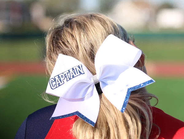 Rear view of a high school cheerleaders bow on her blond head that has captain written on it close up.