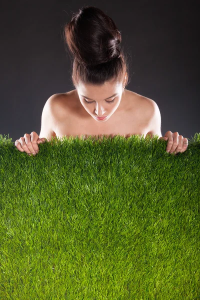 Vrouw en groen gras tegen een donkere achtergrond. — Stockfoto