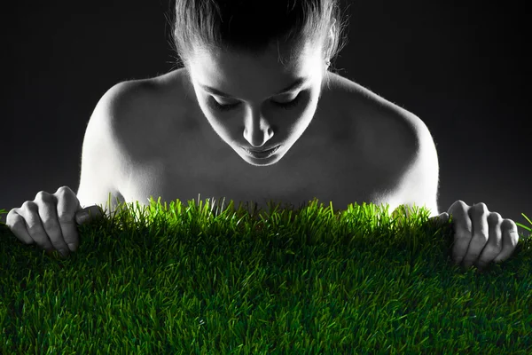 Vrouw en groen gras tegen een donkere achtergrond. — Stockfoto