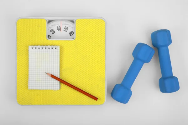 Scales, notebook with pencil and a dumbbell. — Stock Photo, Image