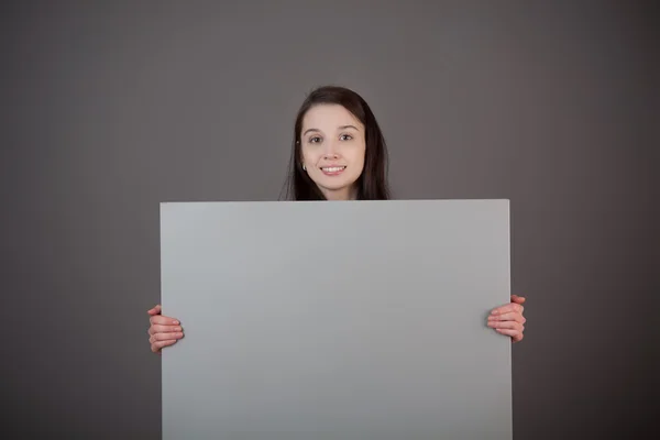 Uma mulher segura uma superfície cinzenta em branco . — Fotografia de Stock