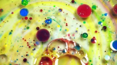 Colorful abstract bubbles and drops are rotating on the yellow and white water surface as macro