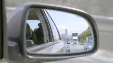 Reflections in the side mirror of a car on the highway. There is a truck in the side mirror