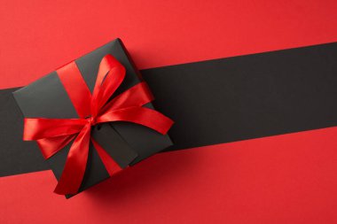 Kopyalama uzayı ile izole edilmiş iki renk kırmızı ve siyah arkaplan üzerinde canlı kırmızı kurdele ile siyah hediye kutusunun üst görünümü