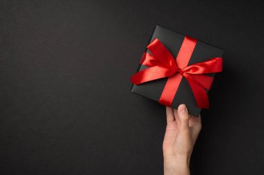 El ele tutuşmanın birinci şahıs görüntüsü şık siyah hediye kutusu ile izole edilmiş siyah arka planda canlı kırmızı kurdele yayıyla