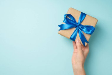 Üstten bakıldığında, kadın el sanatları el sanatları el yapımı kağıt hediye kutusuyla izole edilmiş pastel mavi arka planda canlı mavi saten kurdele yayıyla çekilmiş ilk fotoğraf.