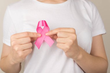 Beyaz tişörtlü kızın göğüs kanseri sembolü olan pembe kurdeleli fotoğrafını çek. Gri arka planda farkındalık.