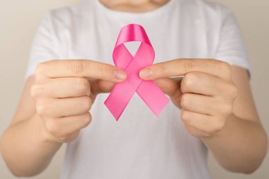 Beyaz tişörtlü kızın göğüs kanseri farkındalığının pembe kurdele sembolünü gösteren yakın plan fotoğrafı.