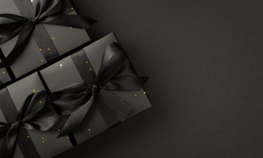 En üstteki fotoğrafta siyah paketler içinde altın pullar ve siyah kurdele ile izole edilmiş siyah zemin üzerinde boş alan ile hediye kutuları var.