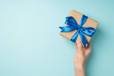 El sanatları el sanatları kağıt hediye kutusunun birinci şahıs görüntüsü canlı mavi saten kurdele yayıyla izole edilmiş pastel mavi arka planda