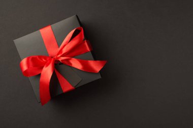 Siyah ambalajlı şık hediye kutusunun en üst görünümü canlı kırmızı saten kurdele ile izole edilmiş siyah arkaplan üzerinde ve telif alanı ile etiketleme