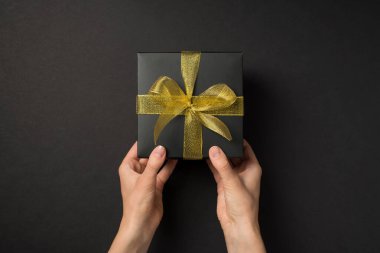 Üstten bakıldığında, izole edilmiş siyah arka planda siyah örgü kurdeleli siyah hediye kutusu tutan ilk kişi.